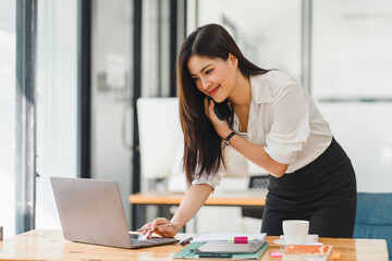 Busy professional woman engages in a phone conversation while using laptop in a contemporary office workspace.