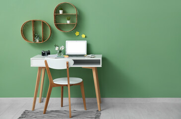 Stylish workplace with laptop and chair near green wall