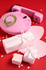 Beautiful gift boxes with paper heart and retro telephone on red background. Valentines Day celebration