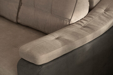 Comfortable quilted soft sofa with a sewn pillow on the armrest in gray-beige colors close-up. Modern upholstered furniture for the home in shadows and blurred background.
