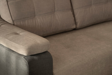 Comfortable quilted soft sofa with a sewn pillow on the armrest in gray-beige colors close-up. Modern upholstered home furniture with stitched pillows and blurred background.
