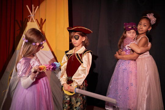 Group of children performing on stage in school play with little boy pirate talking to princess