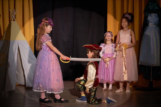 Side view portrait of young girl on stage in school play production acting as warrior princess holding sword and defeating pirate copy space