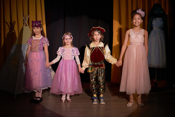 Full length portrait of group of children actors standing on stage holding hands for final bow at school play in theater