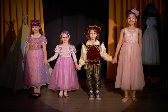 Full length portrait of group of children actors standing on stage holding hands for final bow at school play in theater