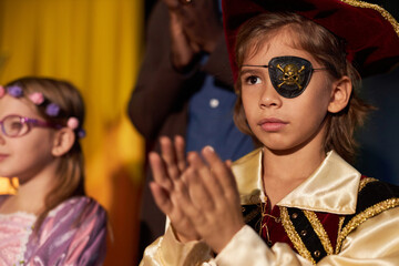 Portrait of young boy wearing pirate costume with eye patch standing on stage in theater and...