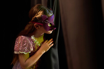 Side view portrait of young girl wearing costume peeking over curtain backstage in theater copy...