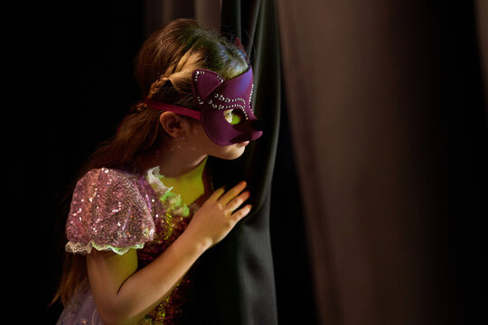 Side view portrait of young girl wearing costume peeking over curtain backstage in theater copy space