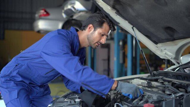 happy latin auto mechanic man checking oil level car in garage cars service. hispanic technician repairing vehicle at garage. inspector writing checklist auto repair shop. engine