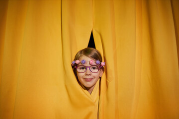 Close up of little girl peeking head on stage from yellow curtains with spotlight, copy space