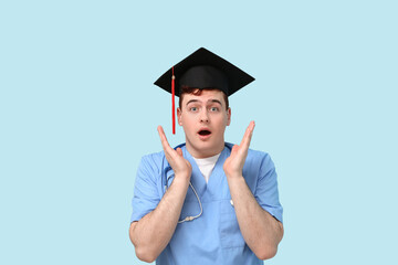 Shocked male student in mortar board and uniform of doctor on blue background