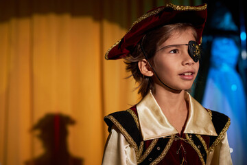 Portrait of young boy wearing pirate costume performing on stage in spotlight, copy space