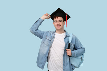 Male student in mortar board with backpack on blue background
