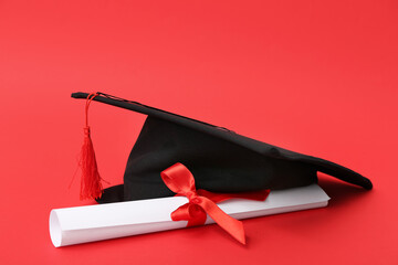 Mortar board and diploma on red background