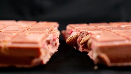 A bar of pink ruby chocolate with freeze-dried strawberries and almonds close-up, isolated black background. A healthy dessert based on berries and nuts