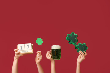 Female hands holding beer, cube calendar, novelty glasses and paper clover on red background. St....