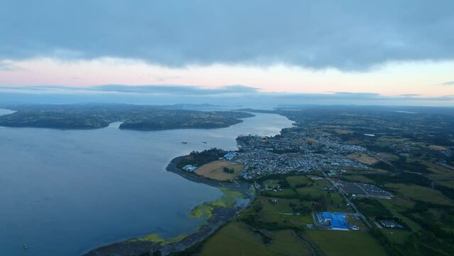 Chilo&eacute; island at dusk, showcasing the vast ocean, quaint towns, and serene landscape, Chonchi in the background, aerial view