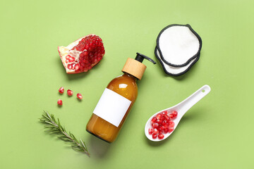 Composition with bottle of cosmetic product, pomegranate and cotton pads on green background