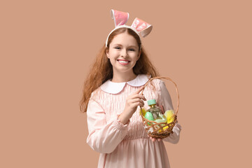 Beautiful young happy woman in bunny ears with wicker basket full of Easter eggs and perfume on brown background