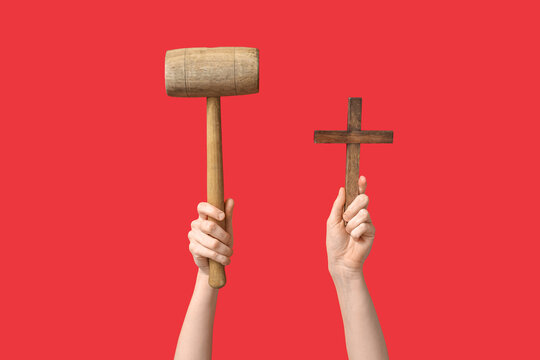 Female hands with wooden mallet and cross on red background. Good Friday concept
