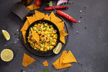 Freshly made mango salsa in a black ceramic bowl and nacho chips