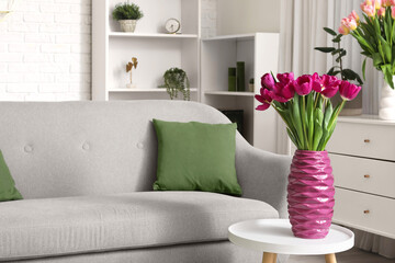 Vase with fresh tulips on table near sofa in living room