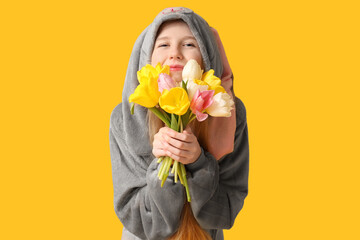 Beautiful young happy woman in bunny costume with bouquet of tulips on yellow background. Easter...