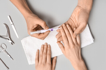 Male manicure master applying cuticle oil onto female fingernails on grey background