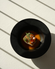 A black bowl filled with food a stew or curry, sauce, vegetables and meat on a white table