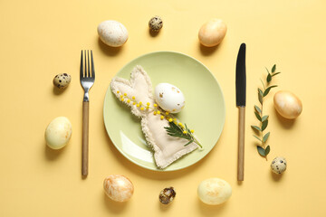 Beautiful table setting with Easter eggs, toy bunny and mimosa flowers on yellow background