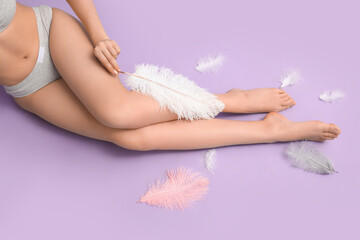 Young woman with soft feathers on lilac background. Epilation concept