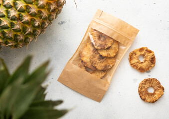 Pack of dried sweet pineapple circles on light background with raw pineapple fruit.Top view.