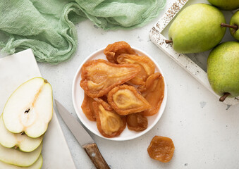 Soft dried sweet  pear slices in plate with green ripe pears and knife on light background.Top view