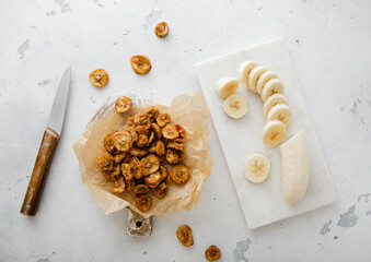 Dried round banana slices with fresh peeled banana and knife.