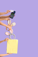 Women with payment terminal, credit card, bunny ears and shopping bag on lilac background. Easter Sale