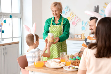 Mature woman giving Easter cake to her little grandson at dinner in kitchen