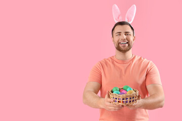 Handsome man in bunny ears with Easter eggs on pink background