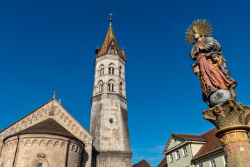Der schiefe Turm der Johanniskirche in der Altstadt von Schwäbisch Gmünd bei sommerlichen Wetter und wolkenlosem Himmel mit der Figur der Mutter Christi des Marienbrunnens auf dem Marktplatz - 748523350