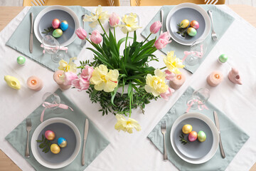 Stylish Easter table setting with flowers, cutlery, candles and painted eggs