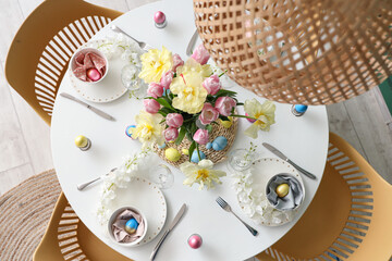 Stylish festive Easter table setting with flowers, cutlery and painted eggs