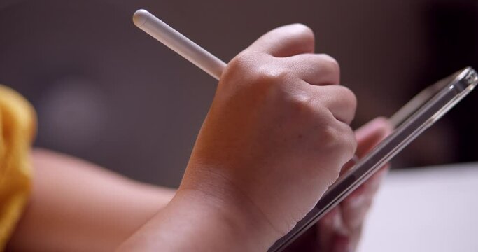 Close-up of an individual scribbling and writing some notes using a portable electronic tablet and a stylus pen.