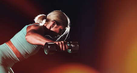 Blonde woman in her mid-fifties training in the gym, photo with flash against a black background.