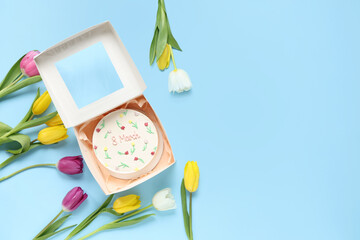 Box with sweet bento cake and beautiful tulips on blue background. International Women's Day