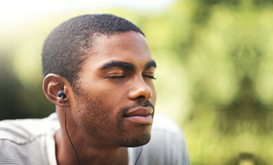 Face, music and relax with black man in garden or park outdoor for summer, peace and quiet. Nature, radio and wellness with calm young person streaming audio or sound on earphones in backyard