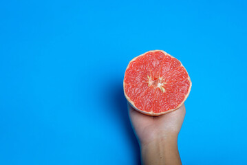 Woman han holding a cut pink grapefruit isolated on blue background. Citrus isolated.