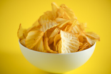 Close-up of potato chips or crisps in bowl against yellow background. perfect for recipes, articles, catalogues, or commercials 