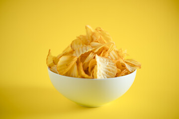 Close-up of potato chips or crisps in bowl against yellow background. perfect for recipes, articles, catalogues, or commercials 