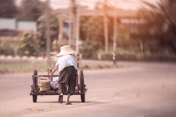 Asian hunchbacked elderly woman wearing a hat works hard on the highway.