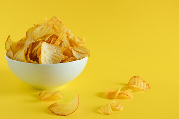 Close-up of potato chips or crisps in bowl against yellow background. perfect for recipes, articles, catalogues, or commercials 
