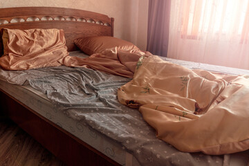Single bed with a blanket and unmade bedclothes in bedroom of home or hotel room in early morning.